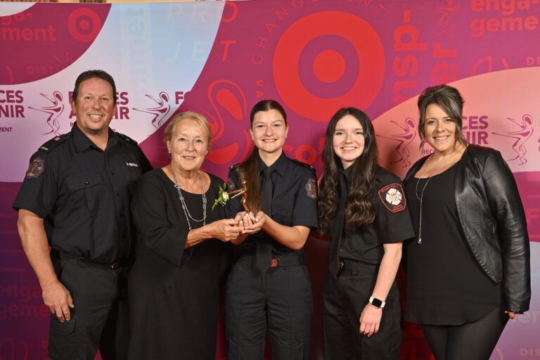 A woman presents an award to two young female firefighters.