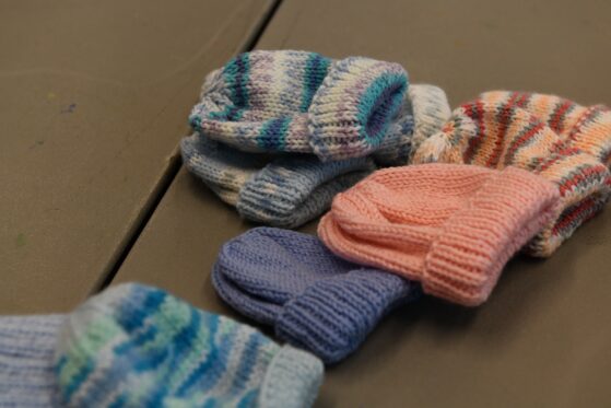 A small pile of hand made knitted or crocheted baby hats sits on a table.